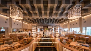 A modern restaurant with a central walkway, wooden furniture, and hanging chandeliers.