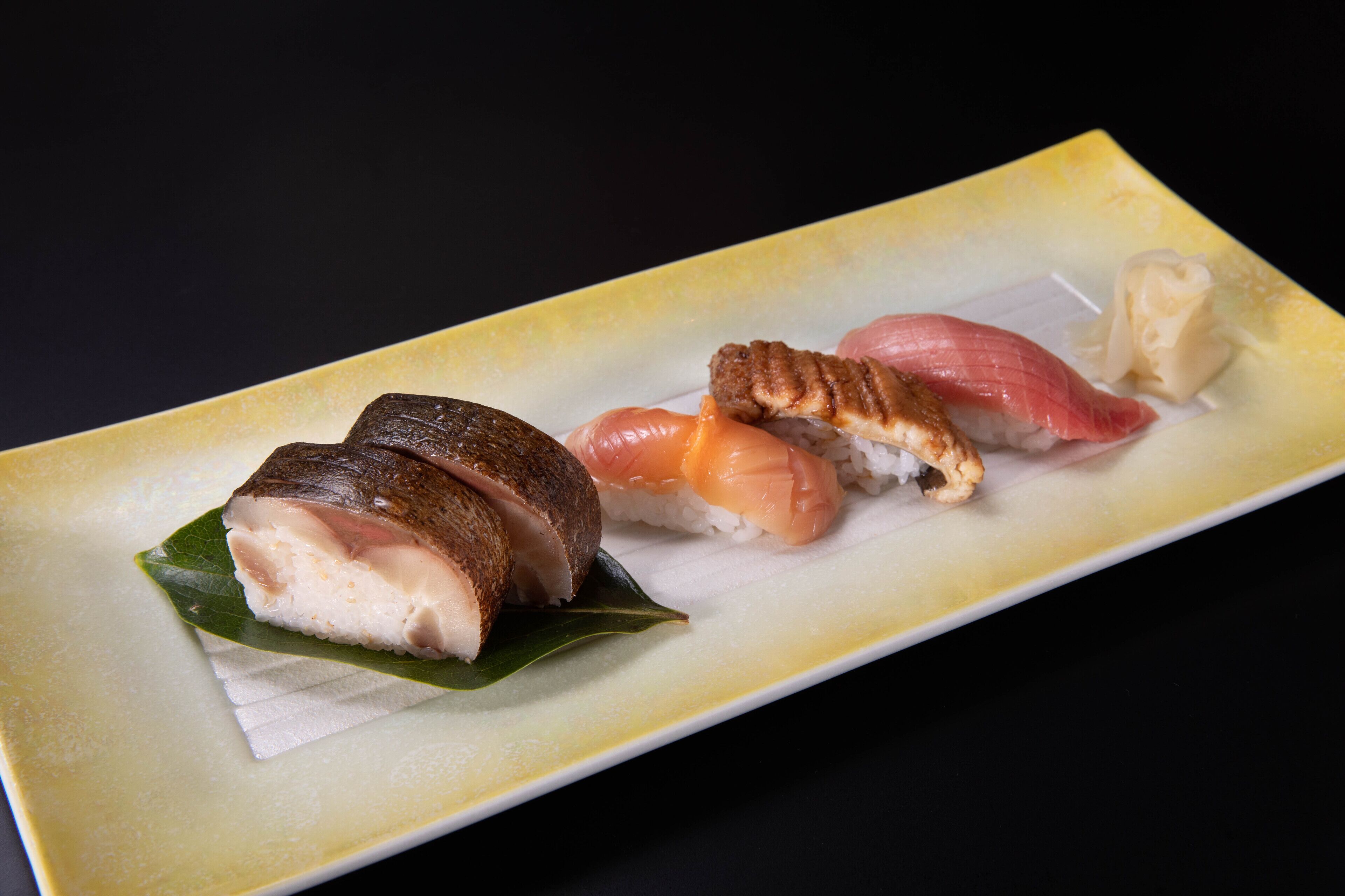 A rectangular plate with four pieces of sushi, including a piece with a leaf garnish.