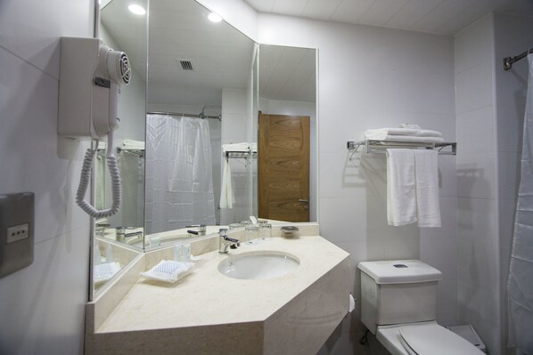 Un baño moderno con un espejo grande, un lavabo blanco, un inodoro y un secador de pelo fijado en la pared.