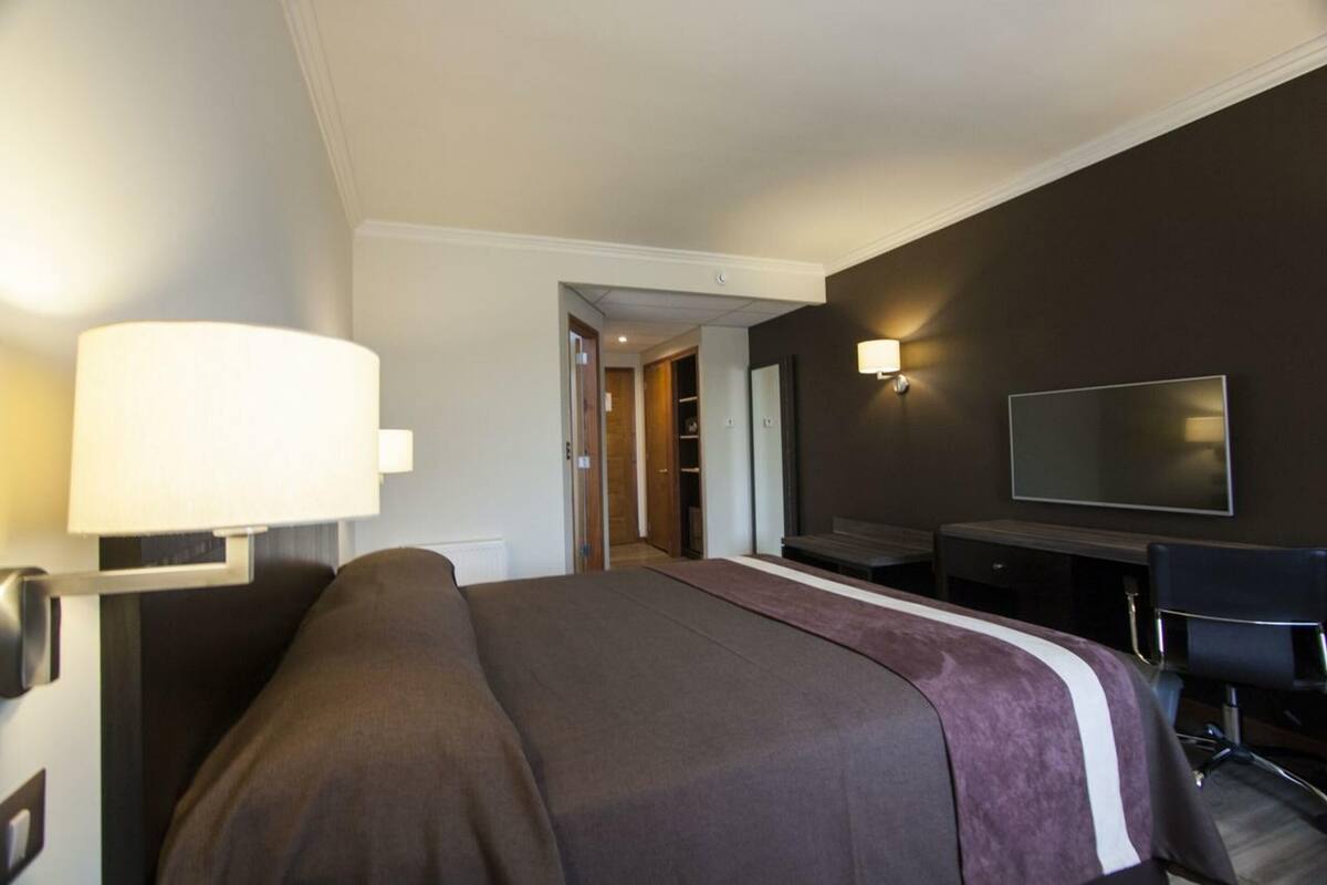 Et hotelværelse med seng, skrivebord med stol, fjernsyn og lampe.