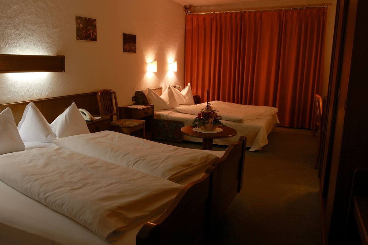 Habitación de hotel con dos camas, una mesita con un florero y una silla.
