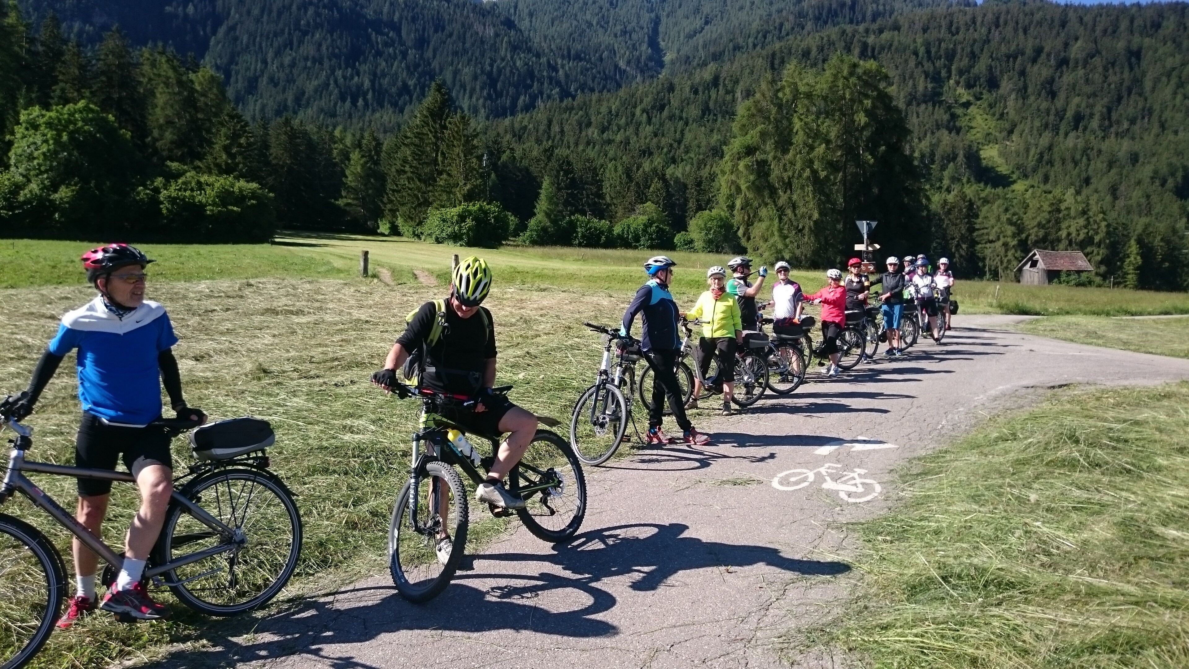 Un grupo de ciclistas en un camino pavimentado con una exuberante montaña al fondo.