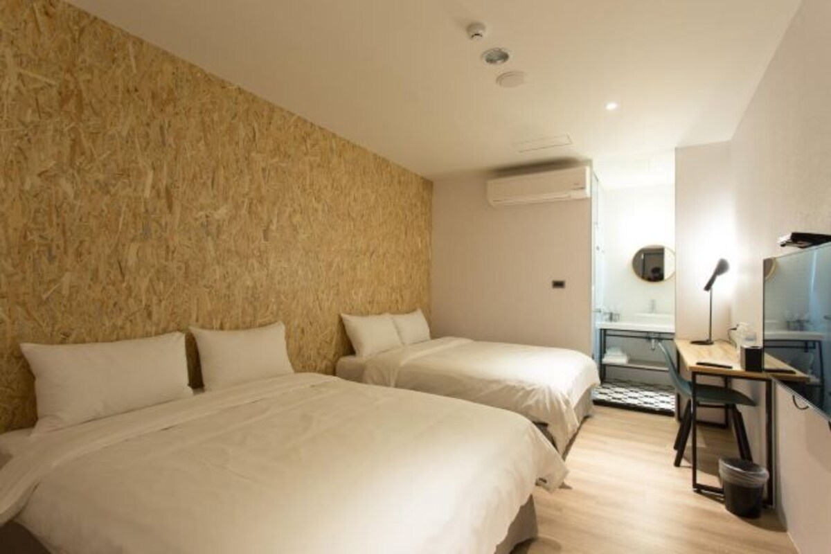 A hotel room with two beds, a desk, a chair, and an air conditioning unit.