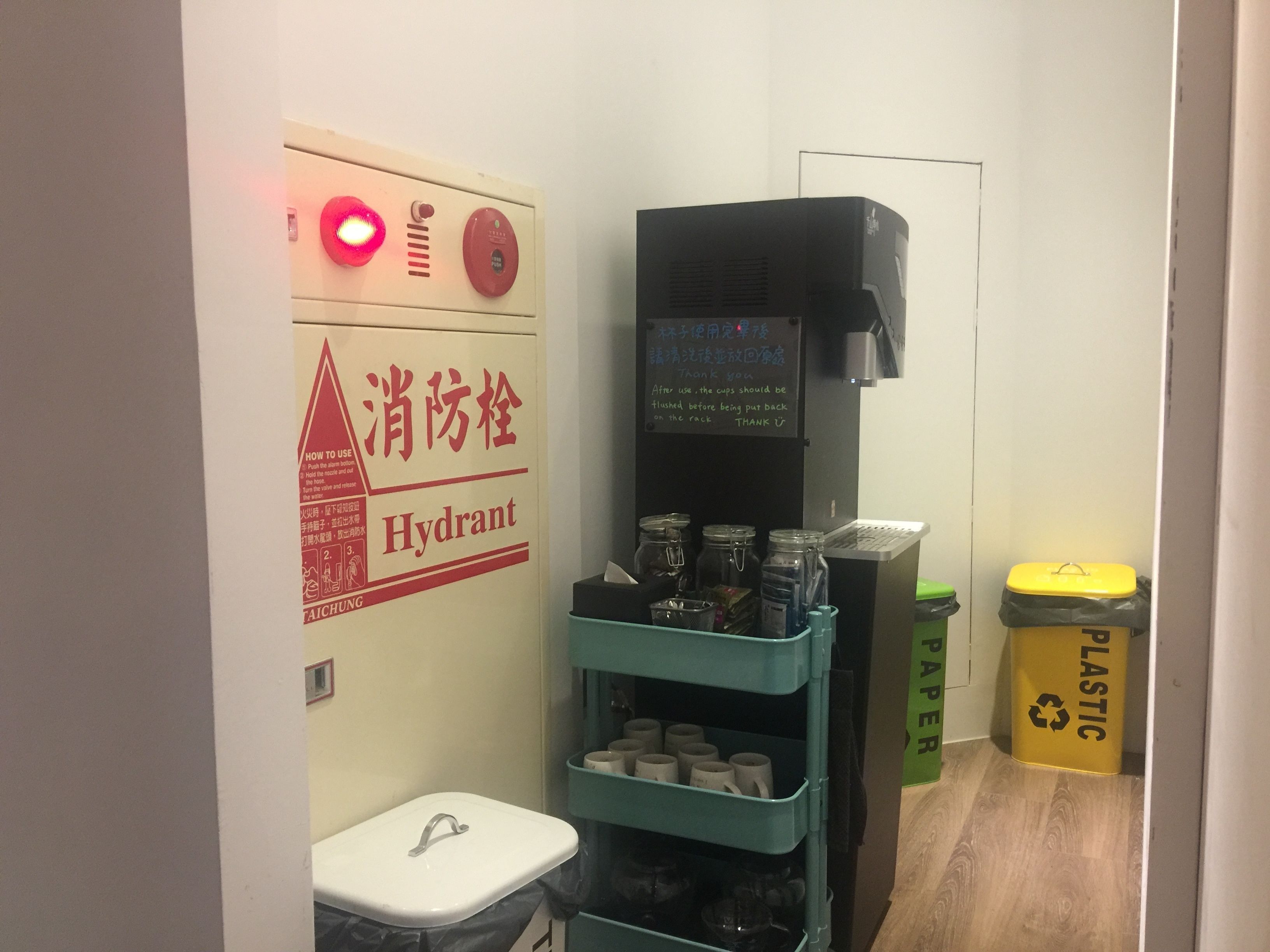 A small room with a sink, a coffee machine, and a trash bin labeled "PLASTIC PAPER".