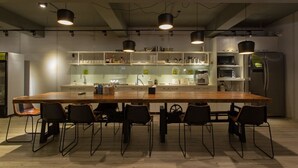 A modern kitchen with a long wooden table and black chairs, equipped with various appliances and shelves. - Let’s Hostel (Kaohsiung)
