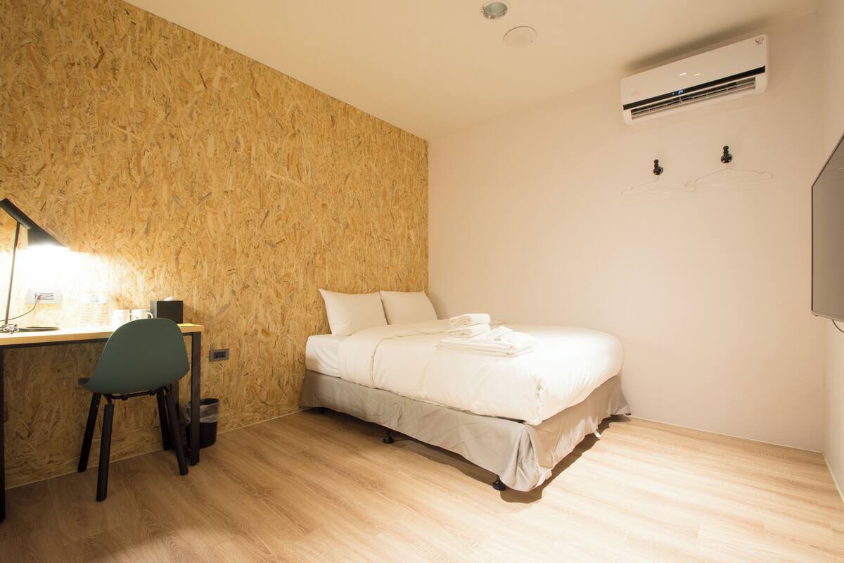 Une chambre avec un mur en bois, un lit, un bureau avec une chaise et un appareil de climatisation.