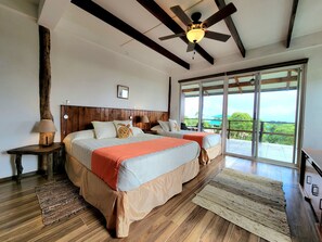 A bedroom with two beds, a ceiling fan, a large window, and a view of the outdoors. - Semilla Verde Boutique Hotel (Bella Vista)