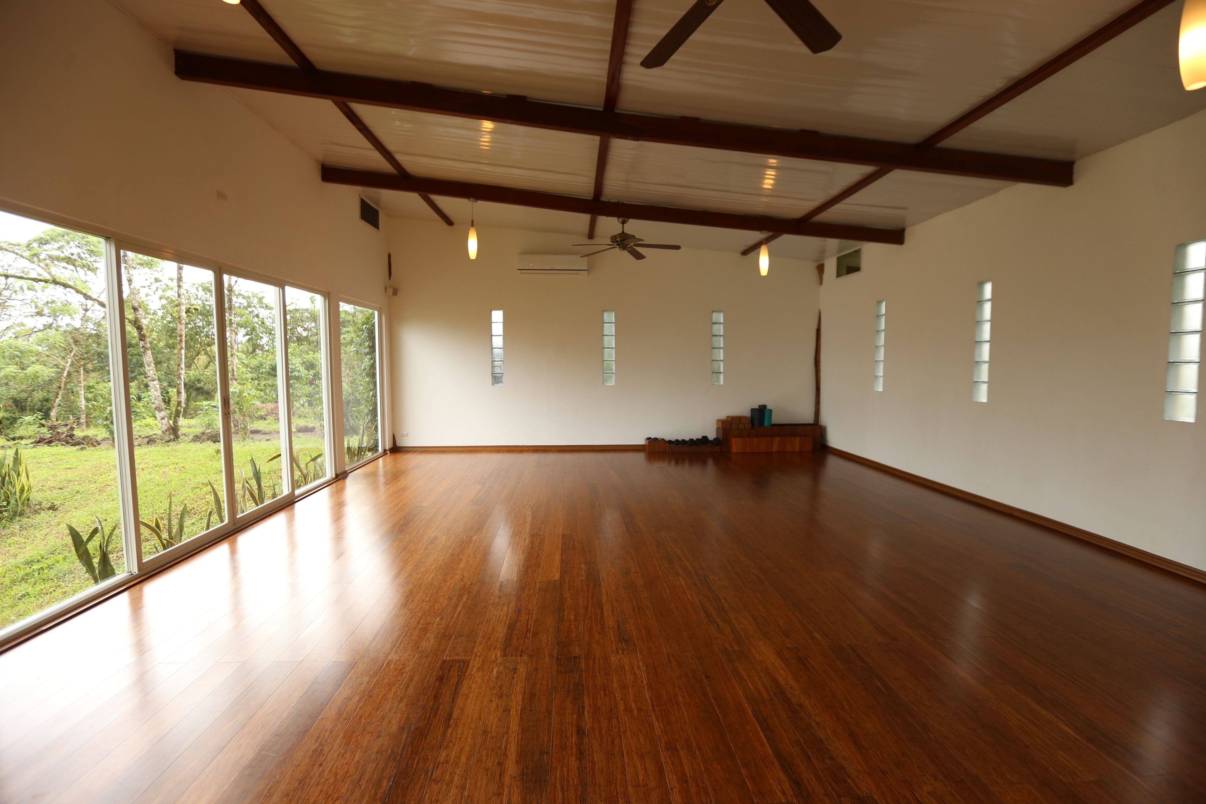 Una habitación amplia con ventanas grandes, suelo de madera y un ventilador de techo.