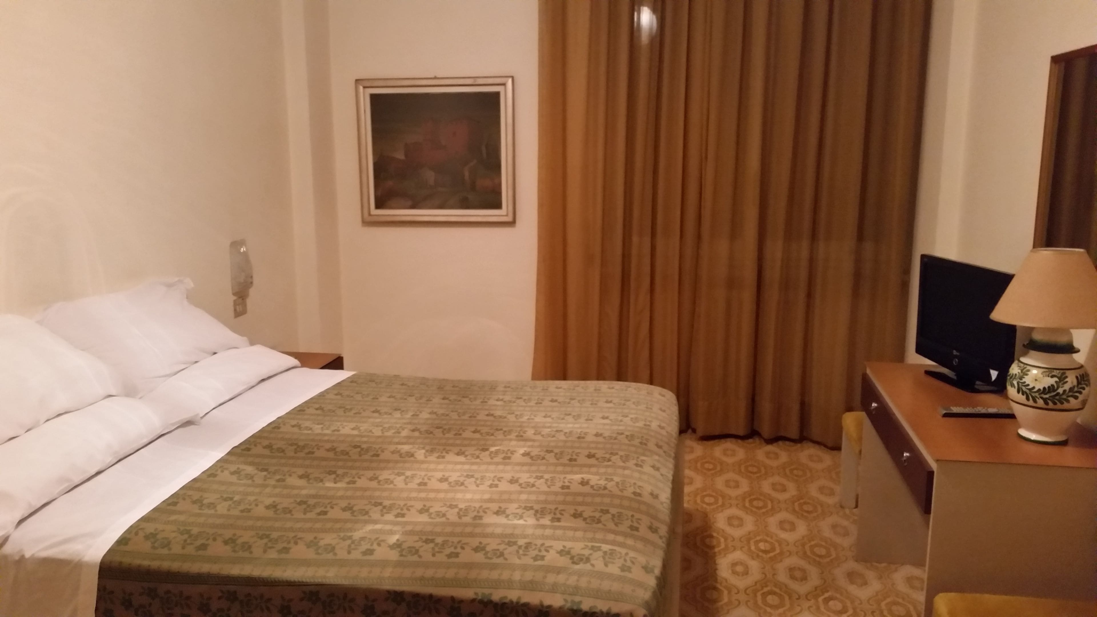 Une chambre d’hôtel avec un lit, un bureau doté d’une lampe, une télévision et un tableau accroché au mur.