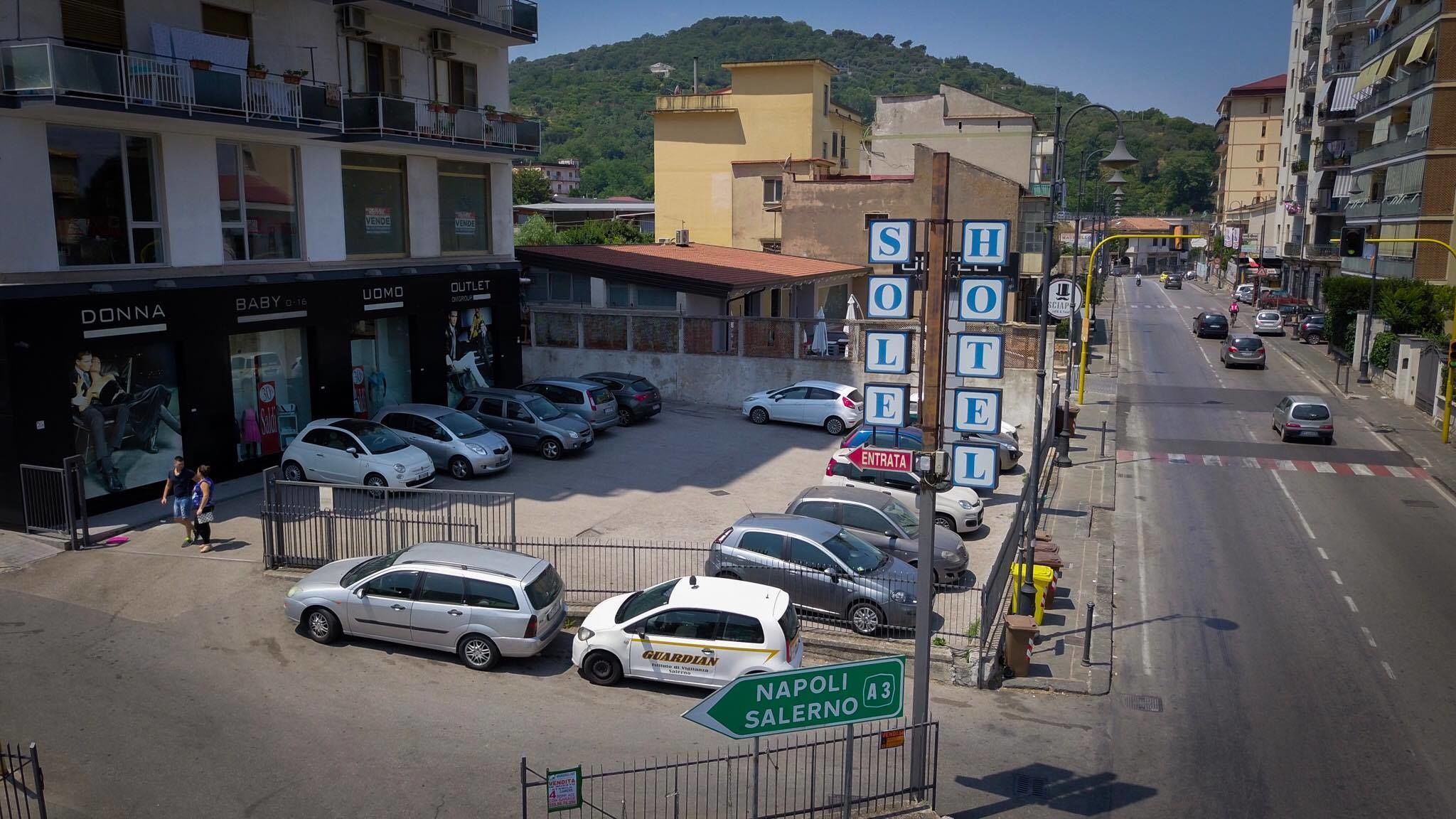 A street view with a row of parked cars, a sign for 'NAPOLI SALERNO A3', and a building with 'OUTLET' signage.