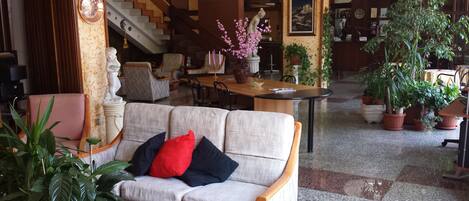 A spacious living area with a sofa, a dining table, and multiple potted plants.