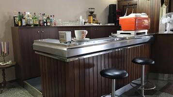 A bar area with a stainless steel counter, two stools, a coffee machine, and various bottles and glasses.