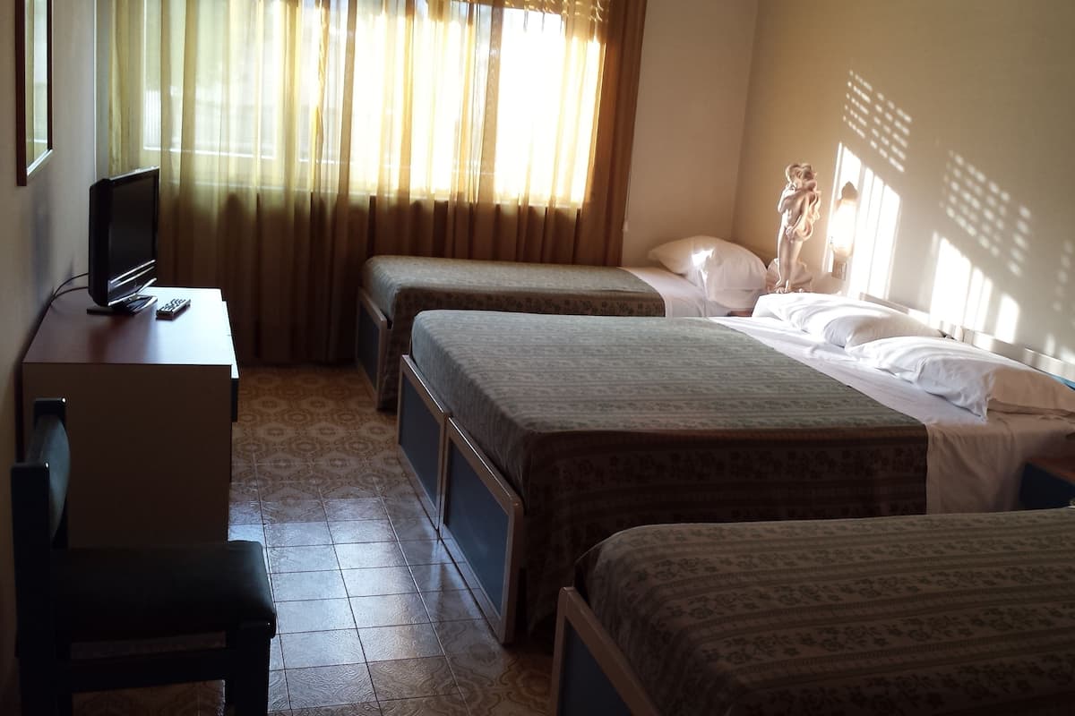A hotel room with two single beds, a desk with a computer, and a window with curtains.