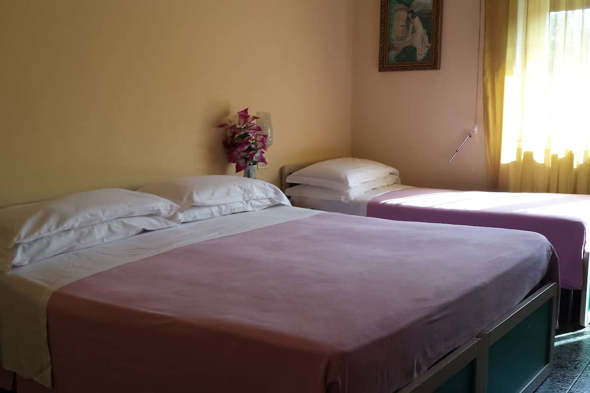 A hotel room with two beds, each with white linens and a pink bedspread. There is a vase with flowers on the nightstand between the beds.