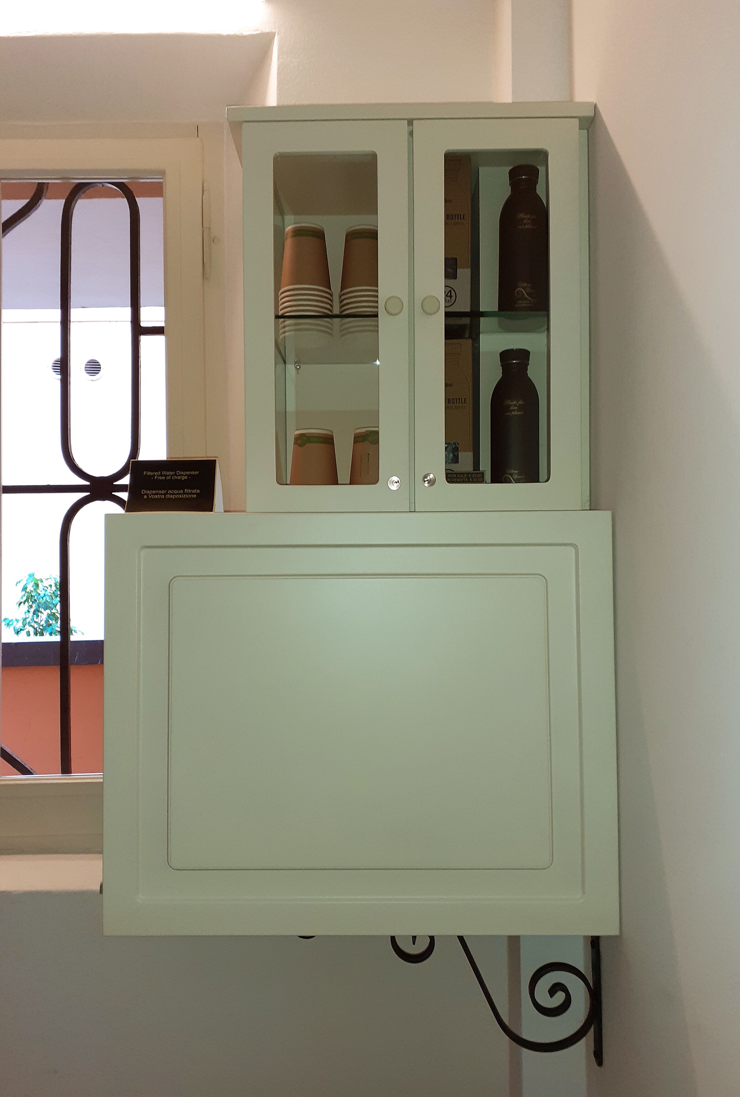 A light green cabinet with two doors, one open revealing stacked plates and a bottle.
