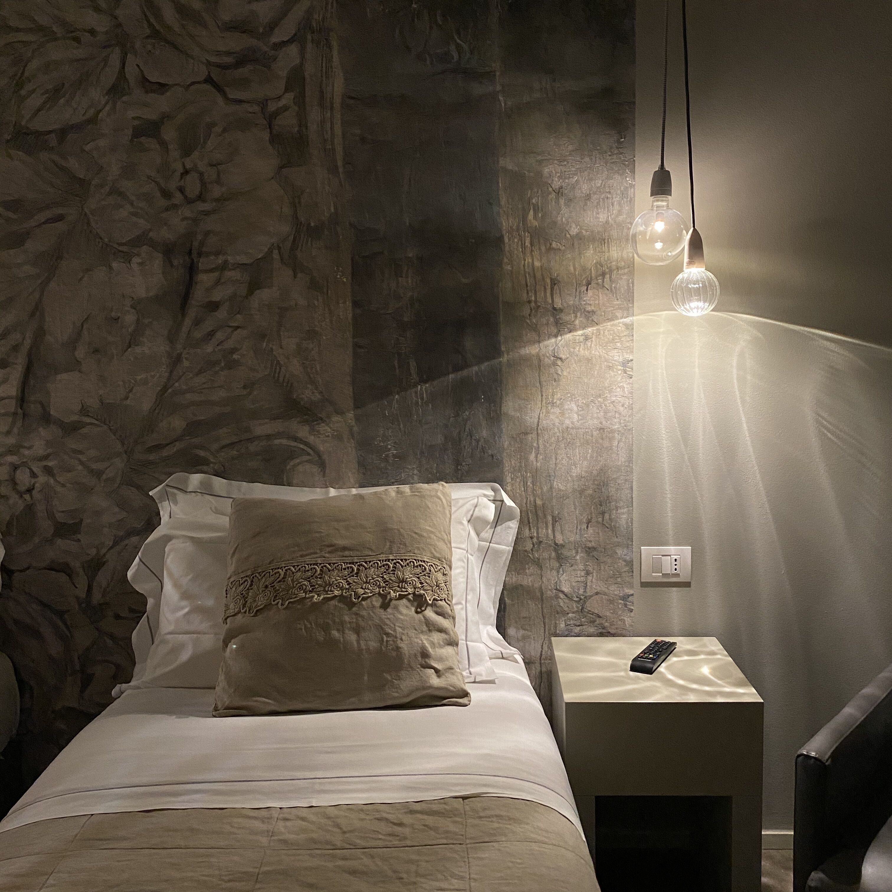 Una cama con un almohadón, una mesita de noche con un control remoto y una pared con textura.
