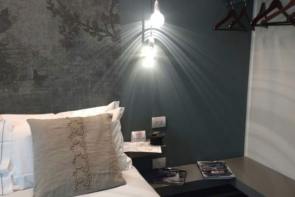A hotel room with a bed, a nightstand with a lamp, a wall with a floral pattern, and a window with curtains.