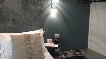 Ein Hotelzimmer mit einem Bett, einem Nachttisch mit Lampe, einer blumengemusterten Wand und einem Fenster mit Vorhängen.