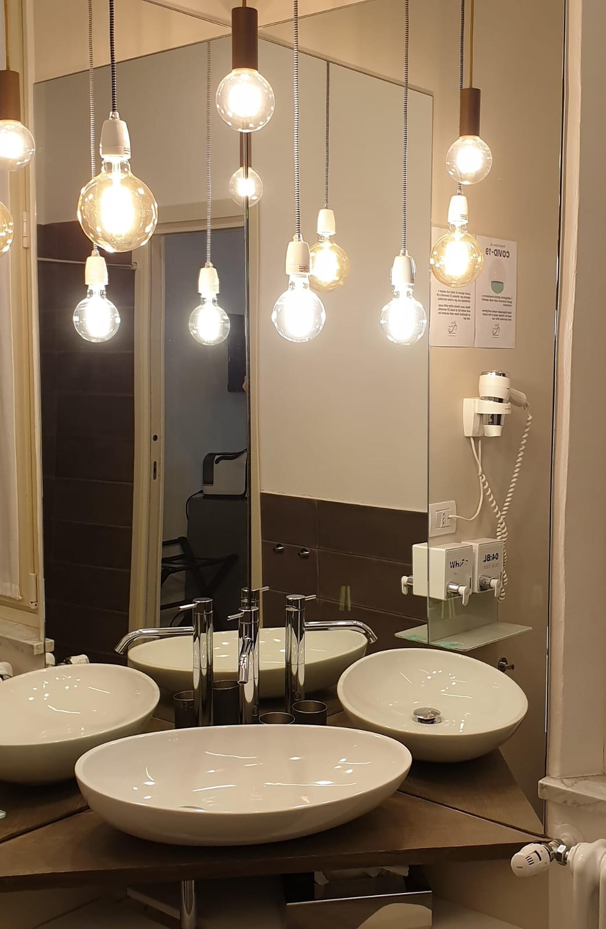 A bathroom with three sinks, a mirror, and pendant lights.