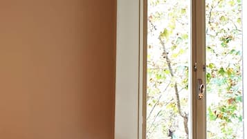 Una habitación con un sofá de color oscuro, un ventanal con vistas a árboles y un piso de baldosas.