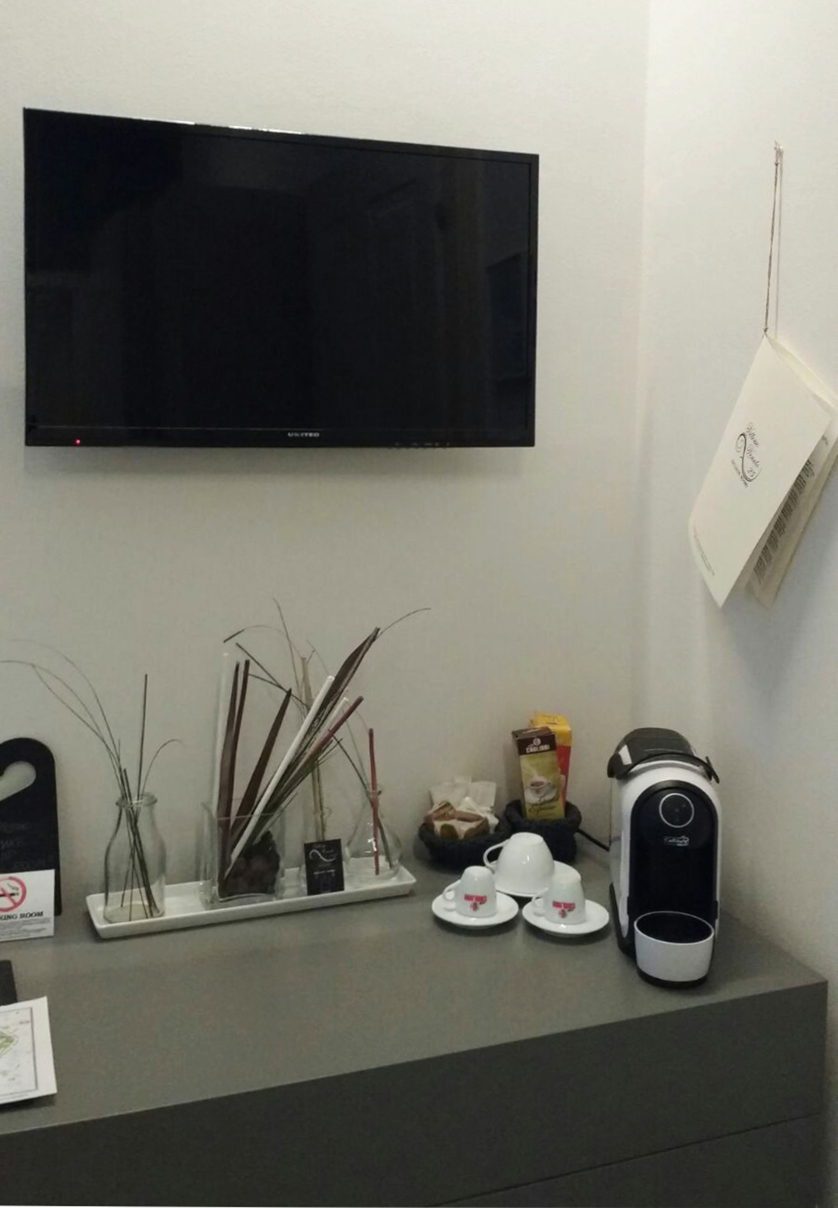 A flat-screen TV mounted on a wall, a coffee maker, and a tray with cups and a box of coffee on a counter.