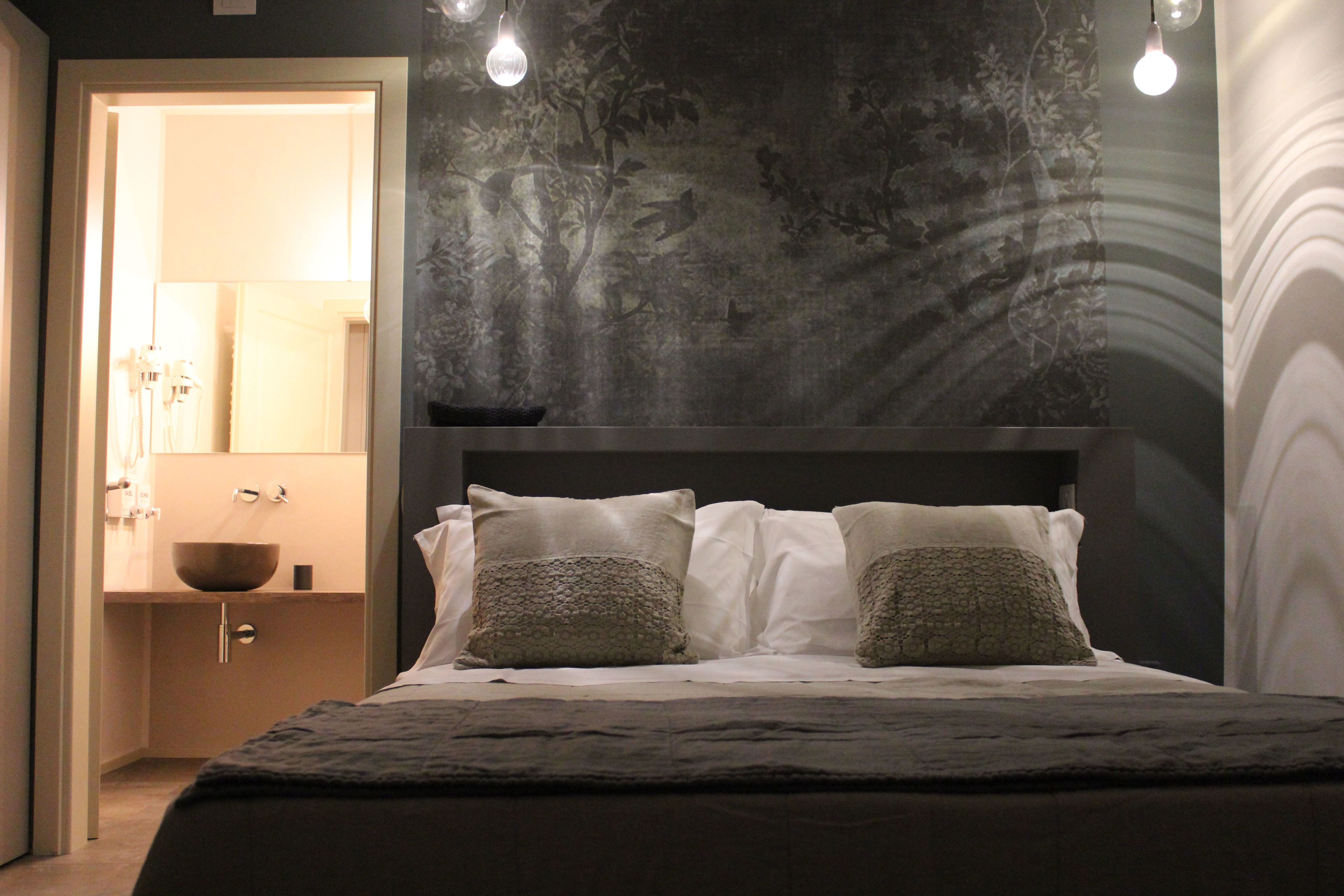 A bedroom with a bed, two pillows, a nightstand, a mirror, and a wall with a tree mural.
