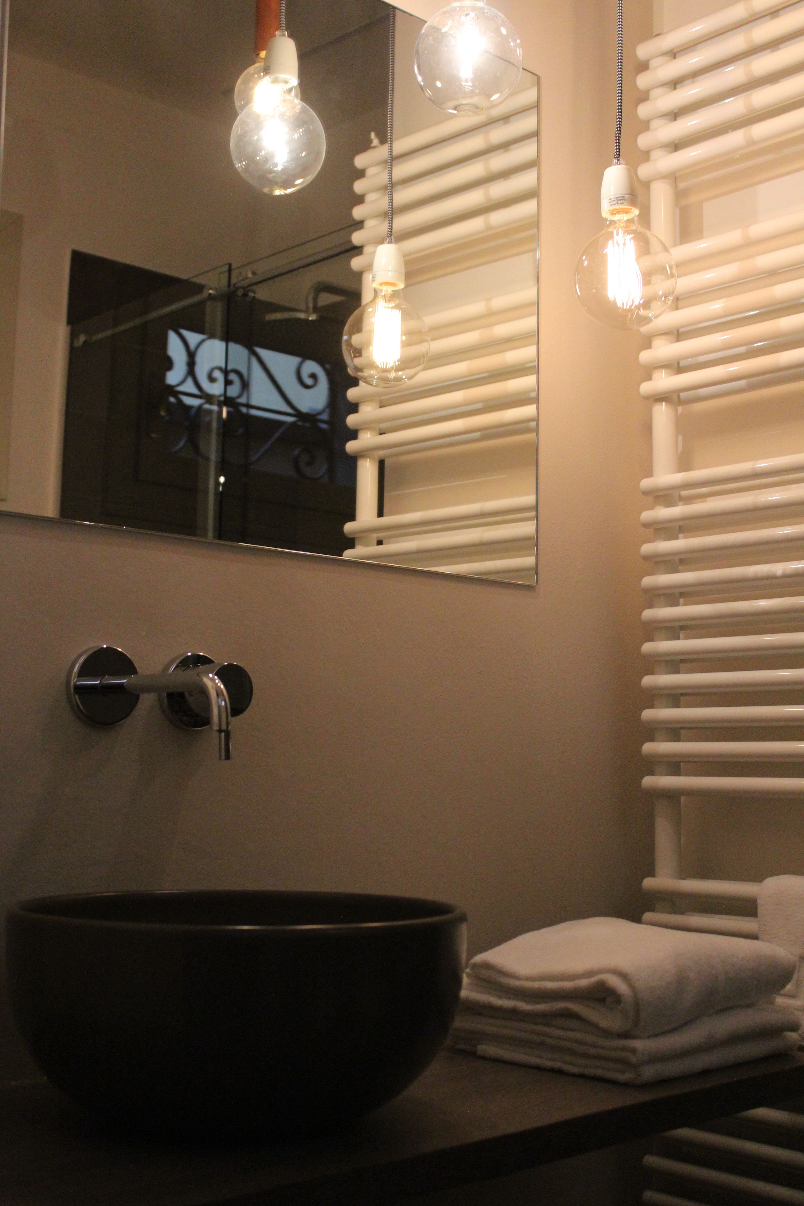 A bathroom with a large mirror, a black vessel sink, and two hanging light fixtures.