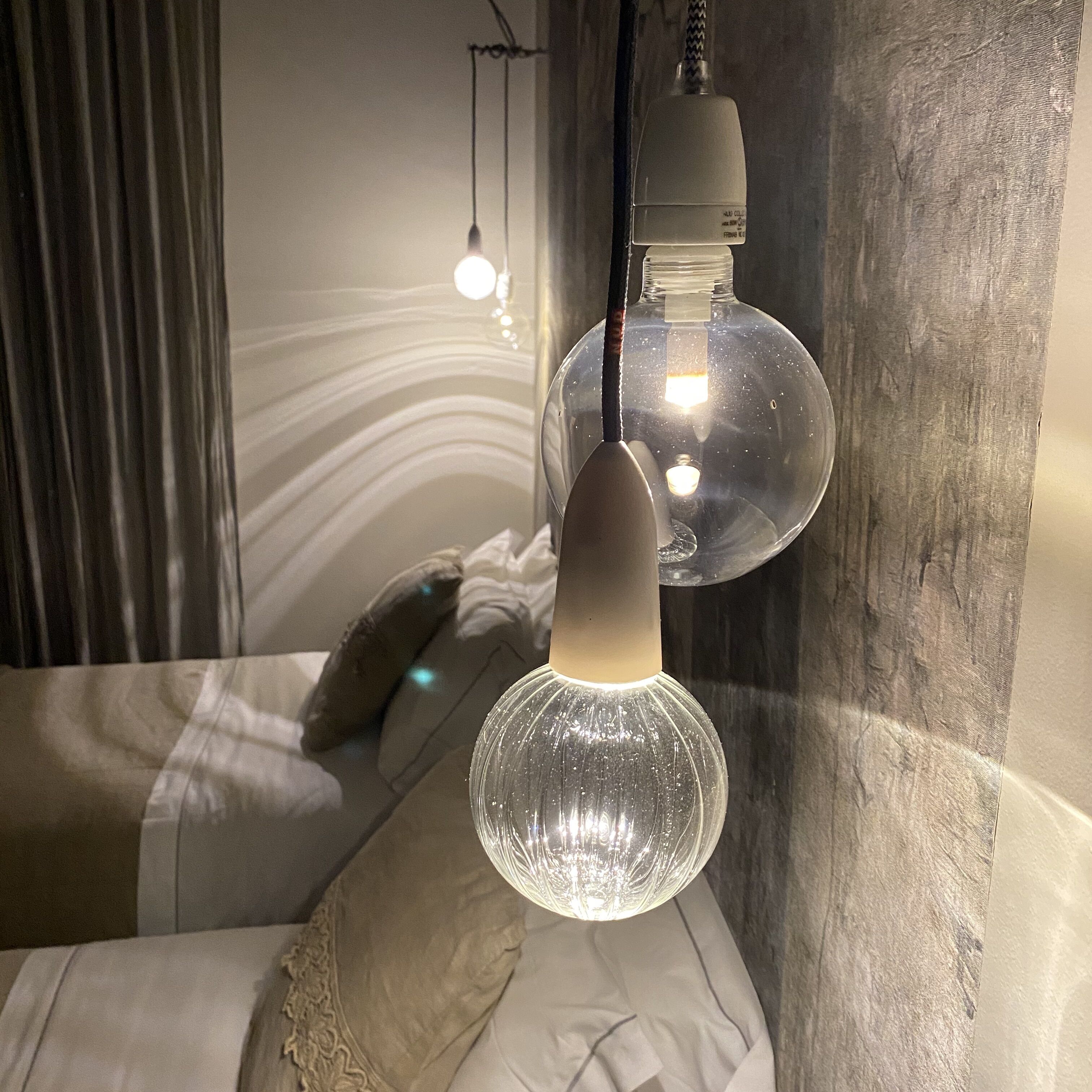 Un dormitorio moderno con cama, lámpara colgante y una lámpara fijada a la pared.