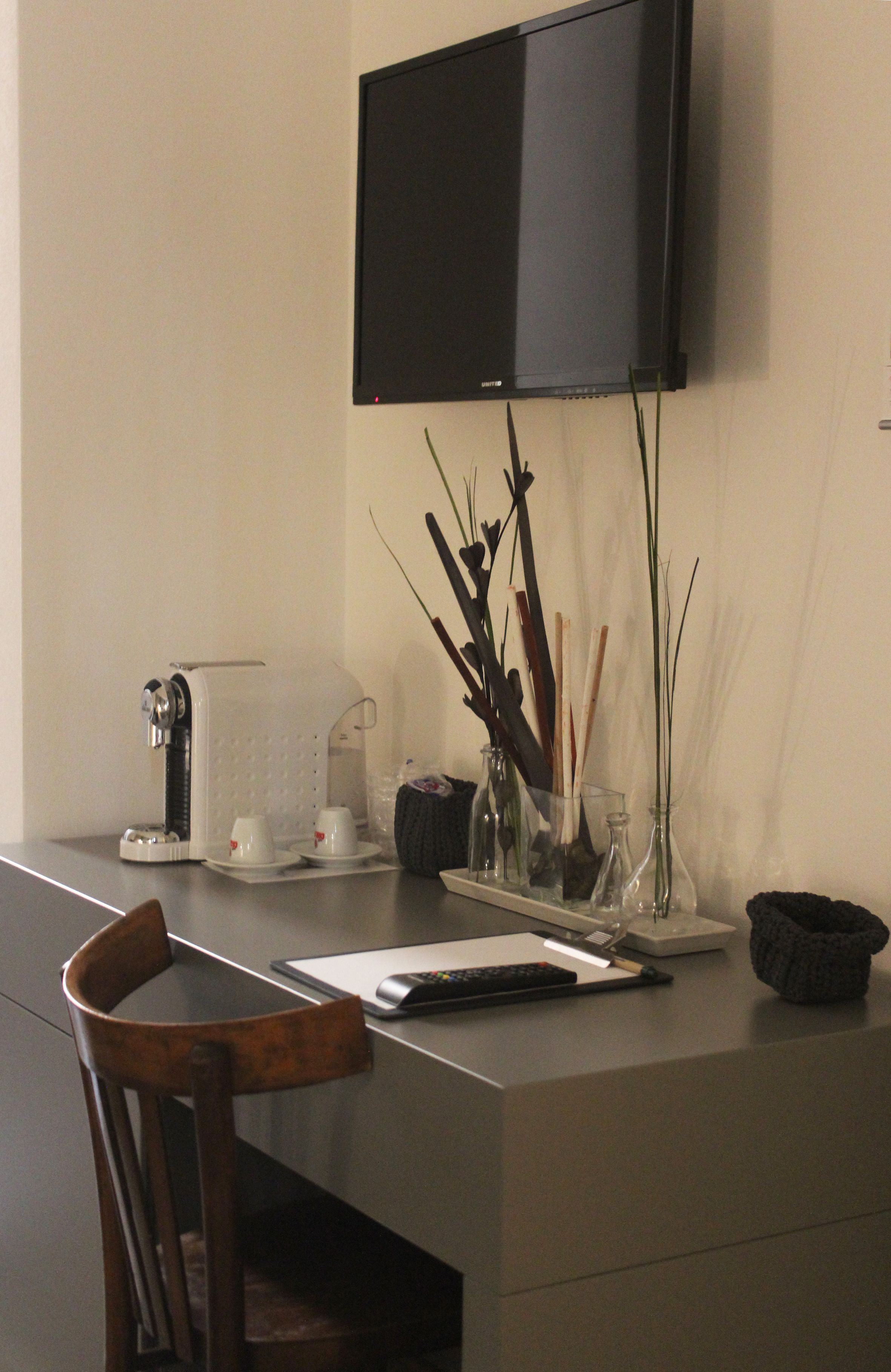 A modern office desk with a flat-screen TV, a coffee maker, and decorative vases.