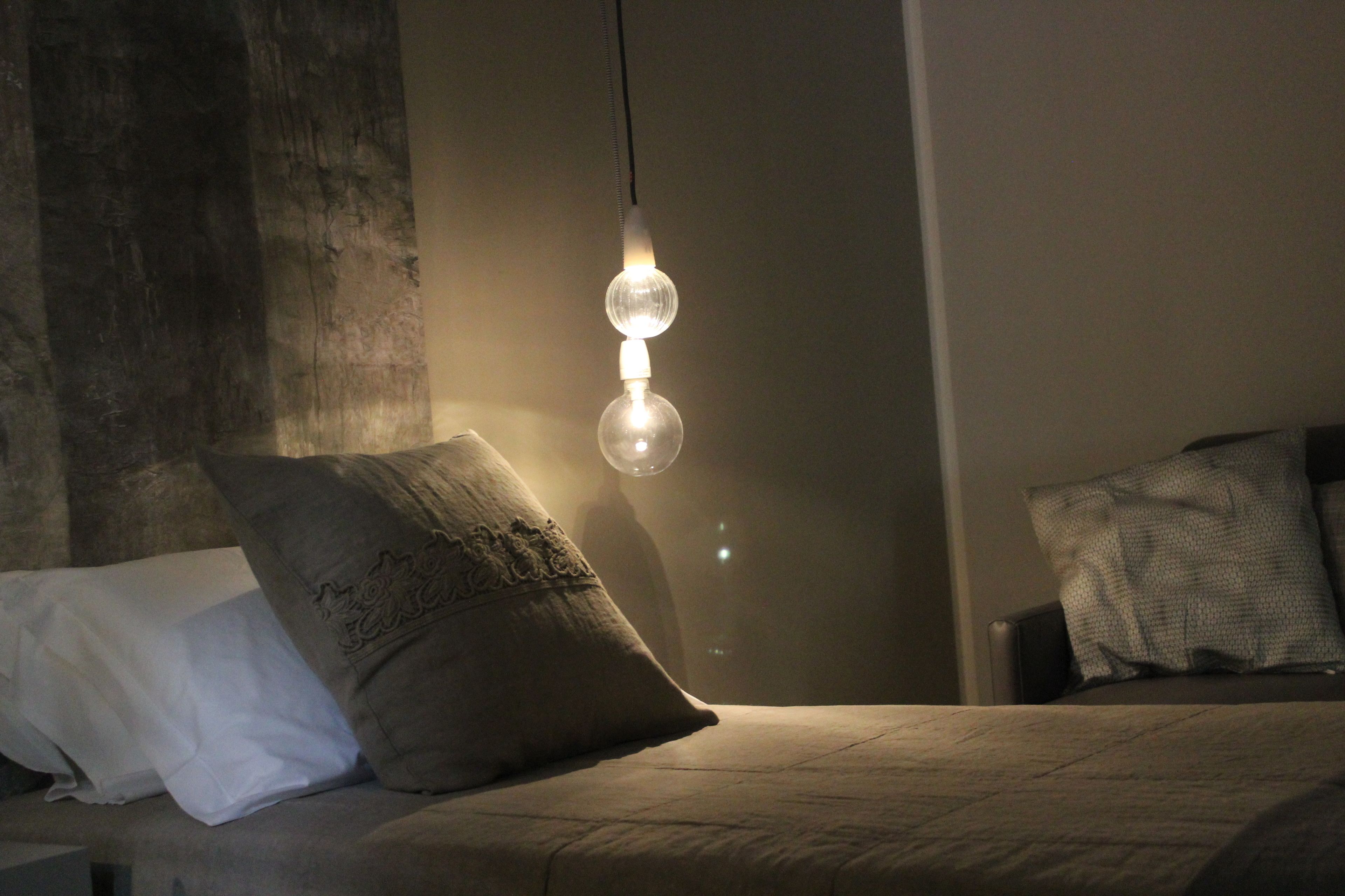 A bedroom with a bed, pillows, and a hanging light fixture.