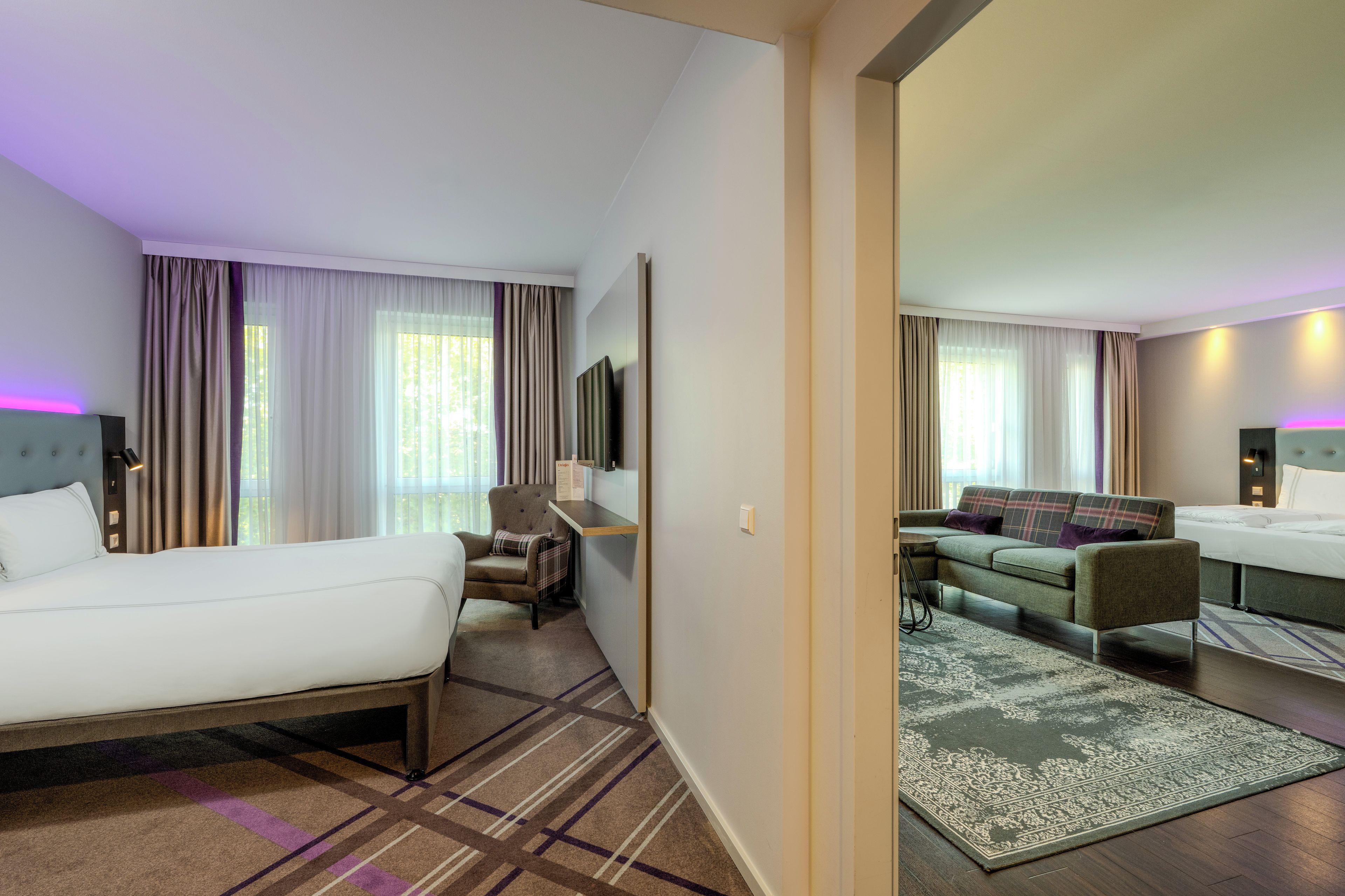 A hotel room with a bed, a desk, a chair, a sofa, and a television.