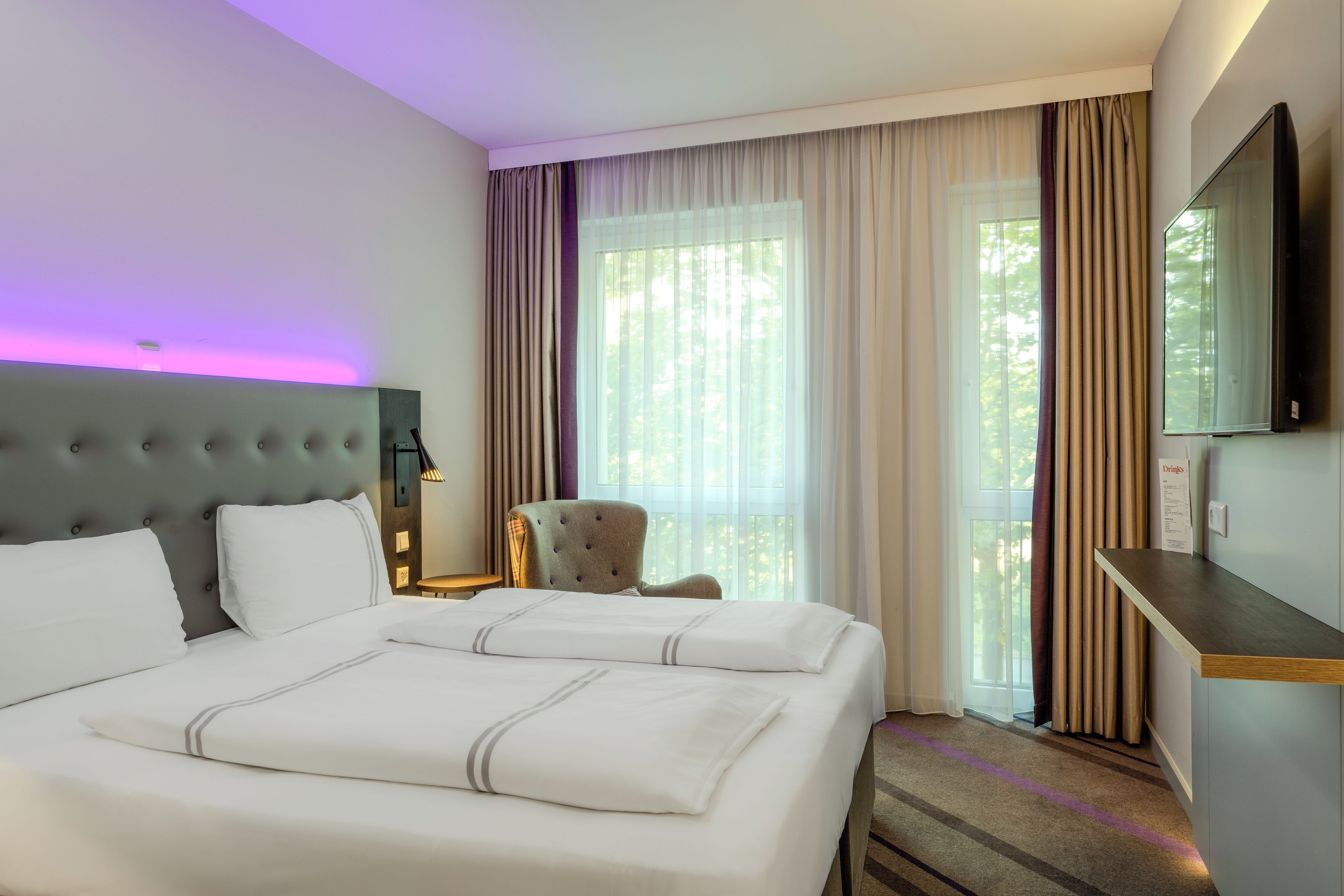 A hotel room with a large bed, a chair, a desk, and a TV.