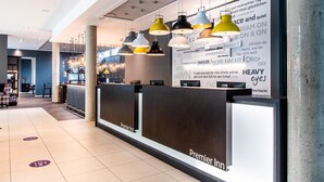A hotel reception area with a modern design, including a reception desk labeled 'Premier Inn,' multiple pendant lights, and a wall with motivational phrases. - Premier Inn Hannover City University (Hannover)