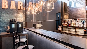A bar with a brick wall, hanging light fixtures, and a well-stocked liquor shelf. - Premier Inn Hannover City University (Hannover)