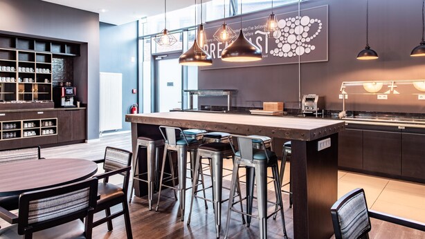 A modern bar area with a central island, bar stools, and pendant lighting. - Premier Inn Hannover City University (Hannover)