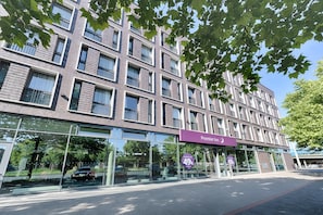 Ein modernes Gebäude mit Glasfassade, einem Schild mit der Aufschrift 'Premier Inn' und einem Parkplatz mit Autos.