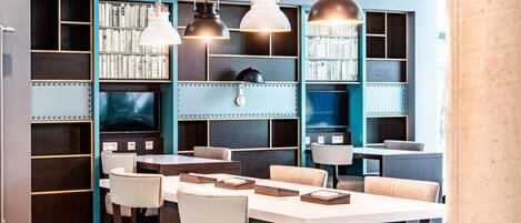 A modern library with bookshelves, tables, chairs, and pendant lighting.
