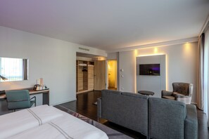 A modern hotel room with a bed, a desk with a lamp, a TV, and a seating area. - Premier Inn Hannover City University (Hannover)