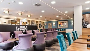 A modern restaurant with purple and teal upholstered chairs, wooden tables, and a central counter. - elaya hotel munich city,  Trademark Collection by Wyndham (Munich)