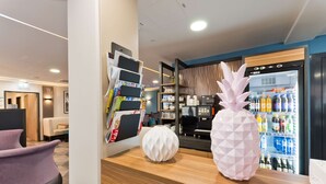 A reception area with a wooden counter, a refrigerator stocked with beverages, and a seating area with a purple chair. - elaya hotel munich city,  Trademark Collection by Wyndham (Munich)