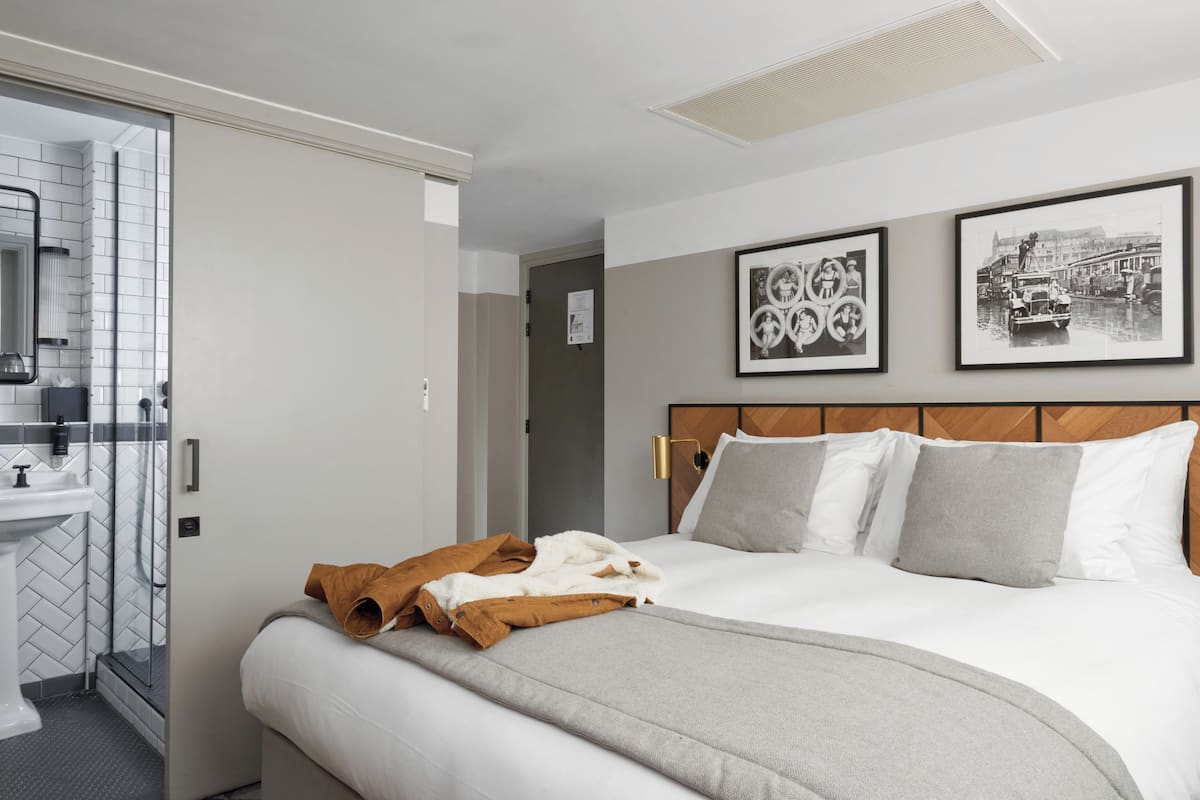 A hotel room with a bed, a bathroom with a sink and mirror, and two framed pictures on the wall.
