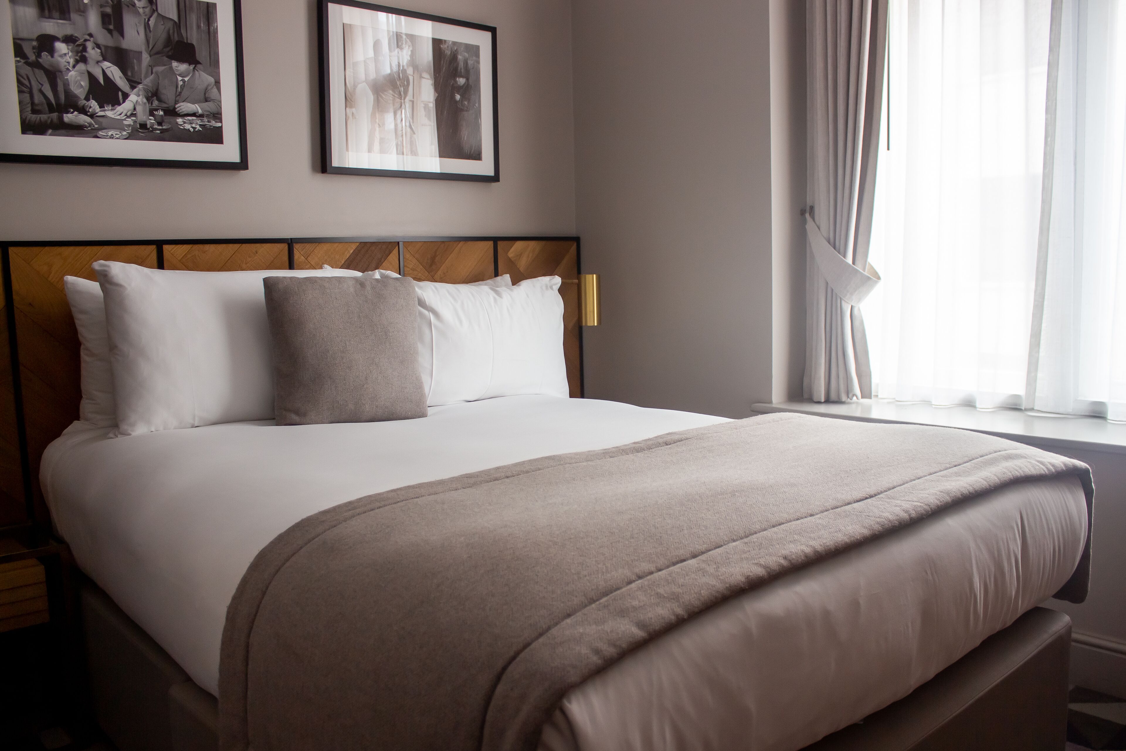 A neatly made bed with a wooden headboard, white bedding, and a beige throw blanket. There are two framed pictures on the wall above the bed.