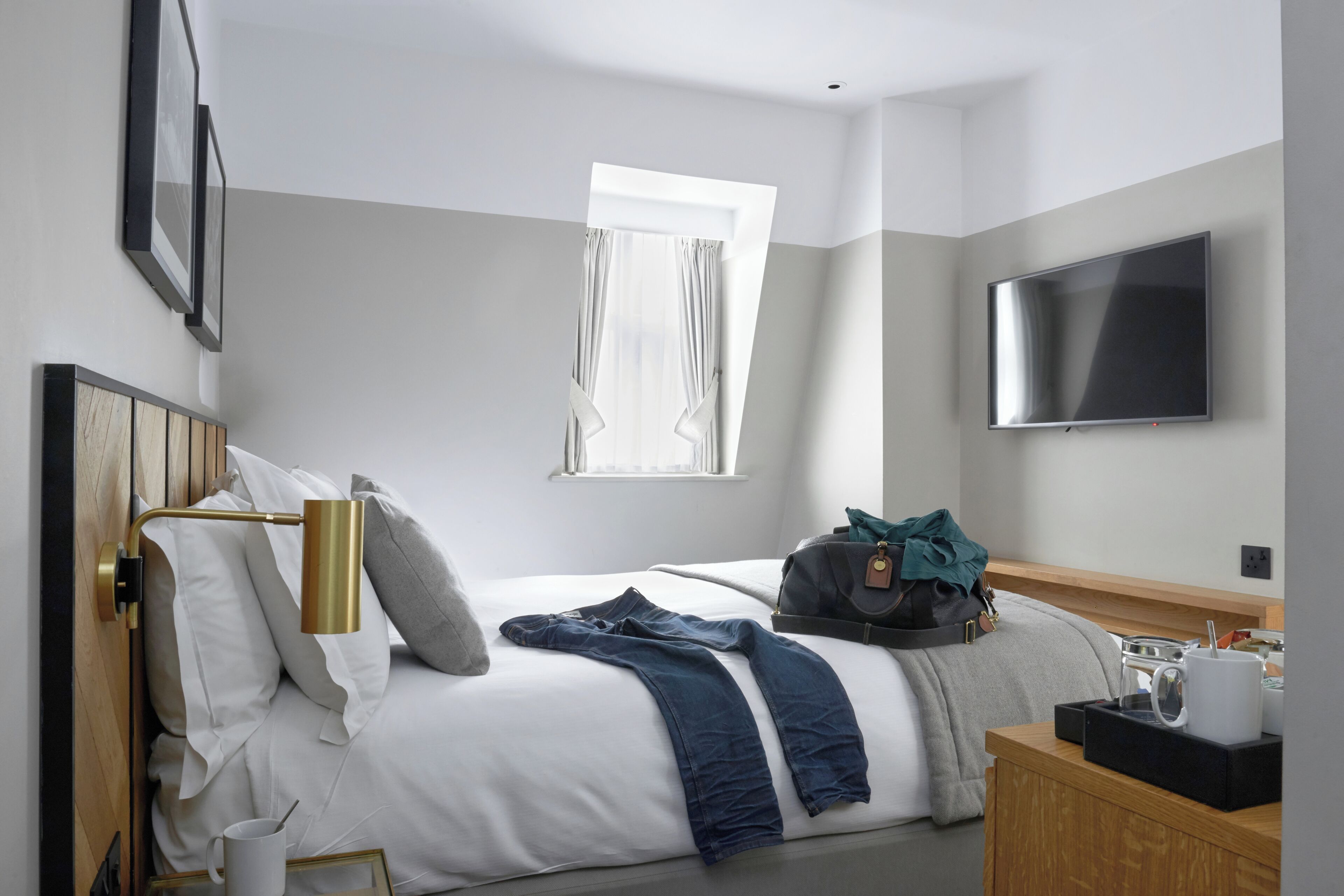 A hotel room with a bed, a TV, a window, and a bedside table.