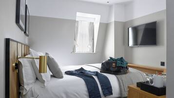 A hotel room with a bed, a TV, a window, and a bedside table.