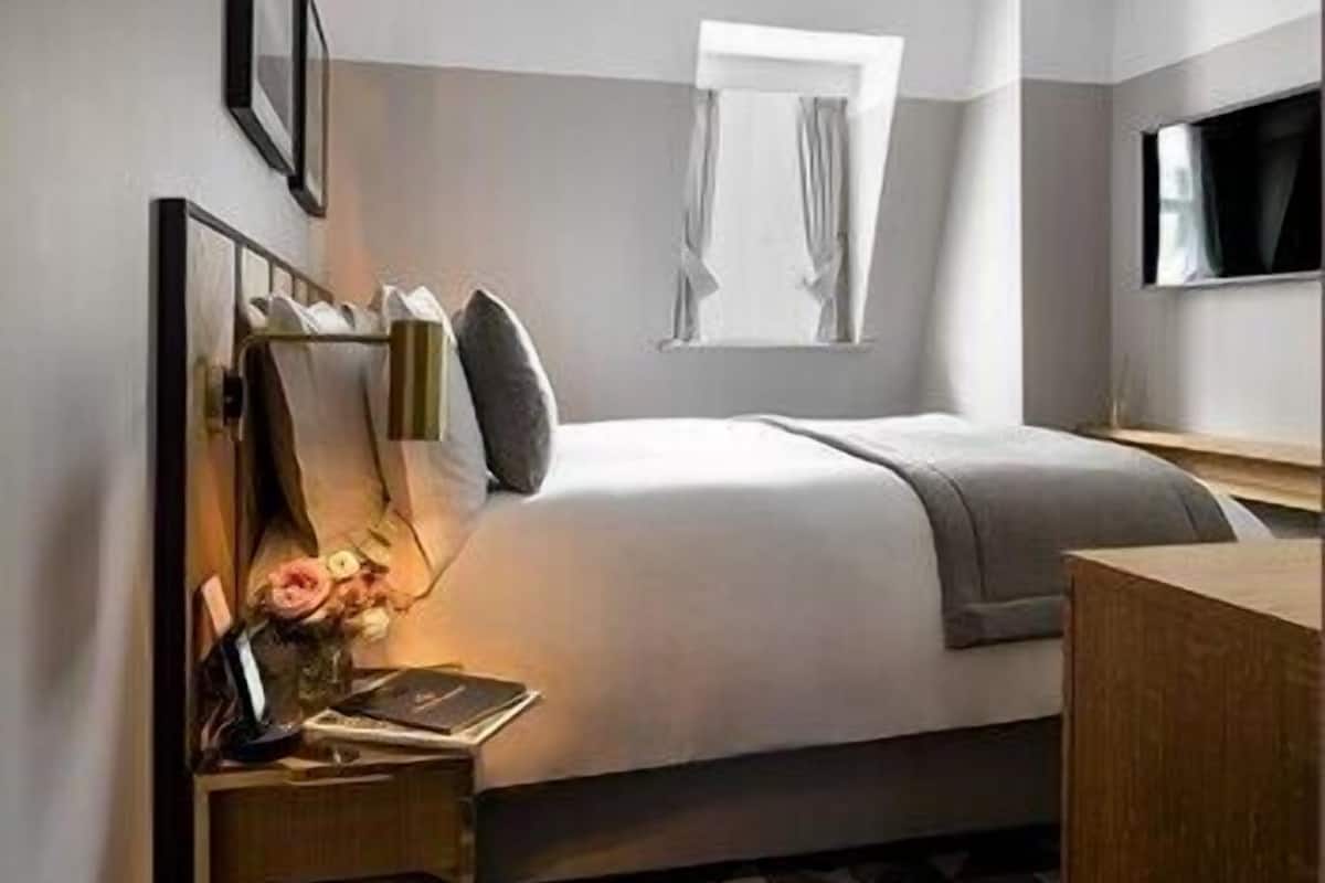 A hotel room with a bed, bedside table, lamp, and a TV mounted on the wall.
