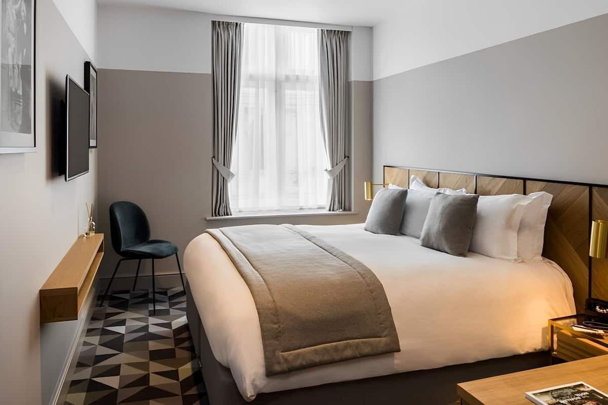 A modern hotel room with a large bed, a desk, a chair, and a TV on the wall.
