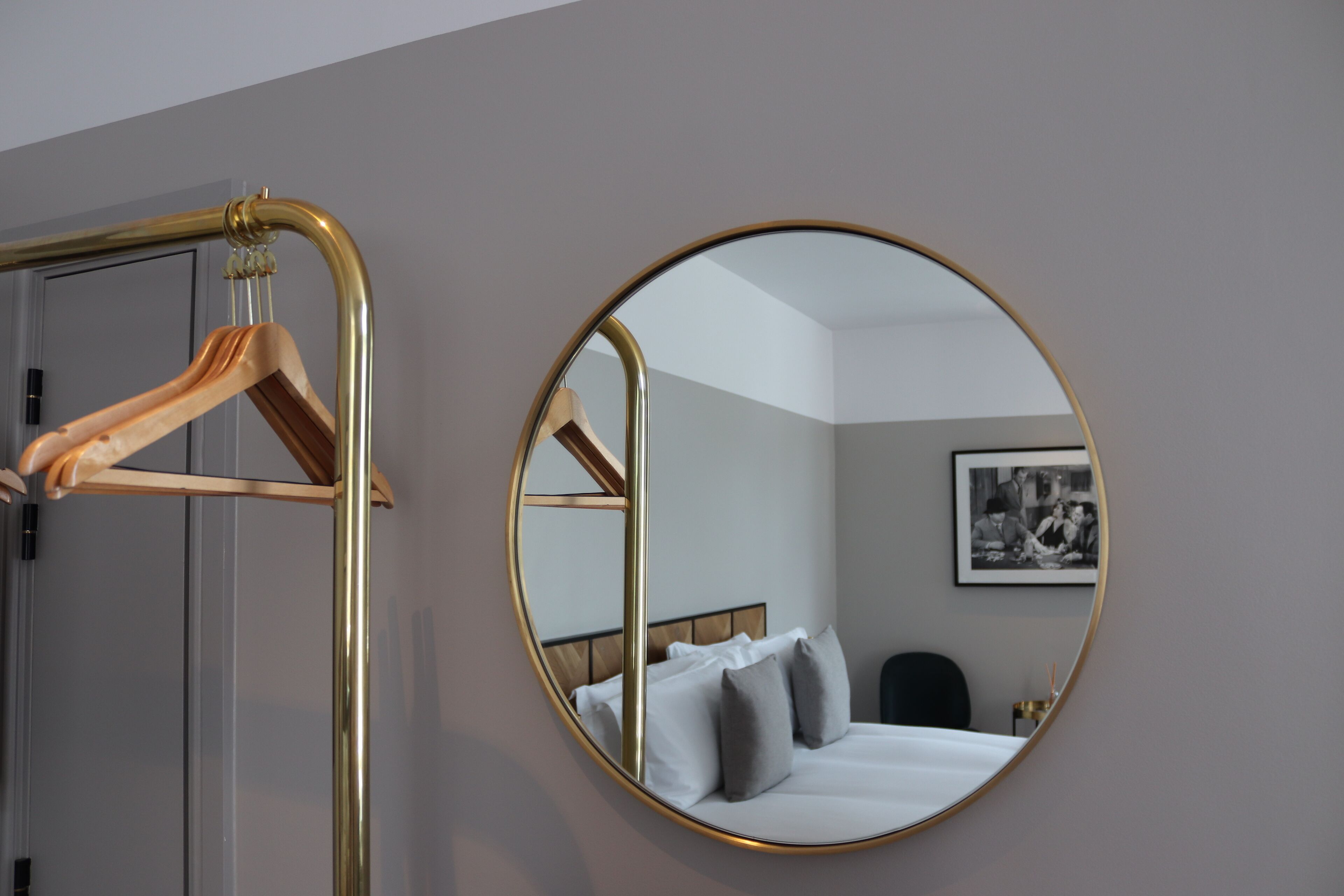 A hotel room with a bed, a round mirror, and a wooden hanger.