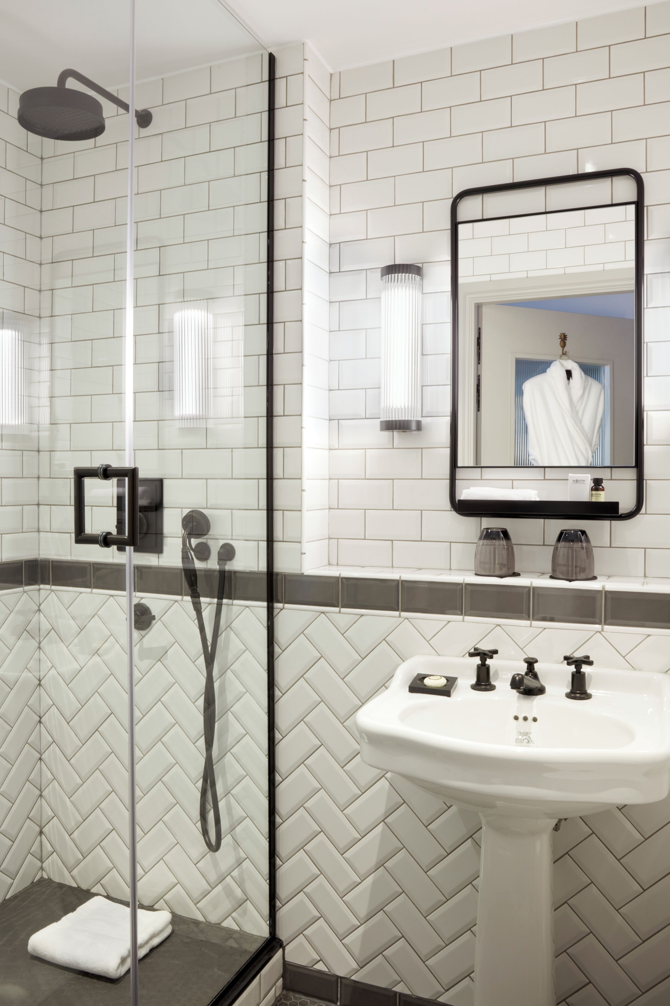 Un baño moderno con ducha de vidrio, un lavamanos blanco con grifo negro y un espejo con marco negro.
