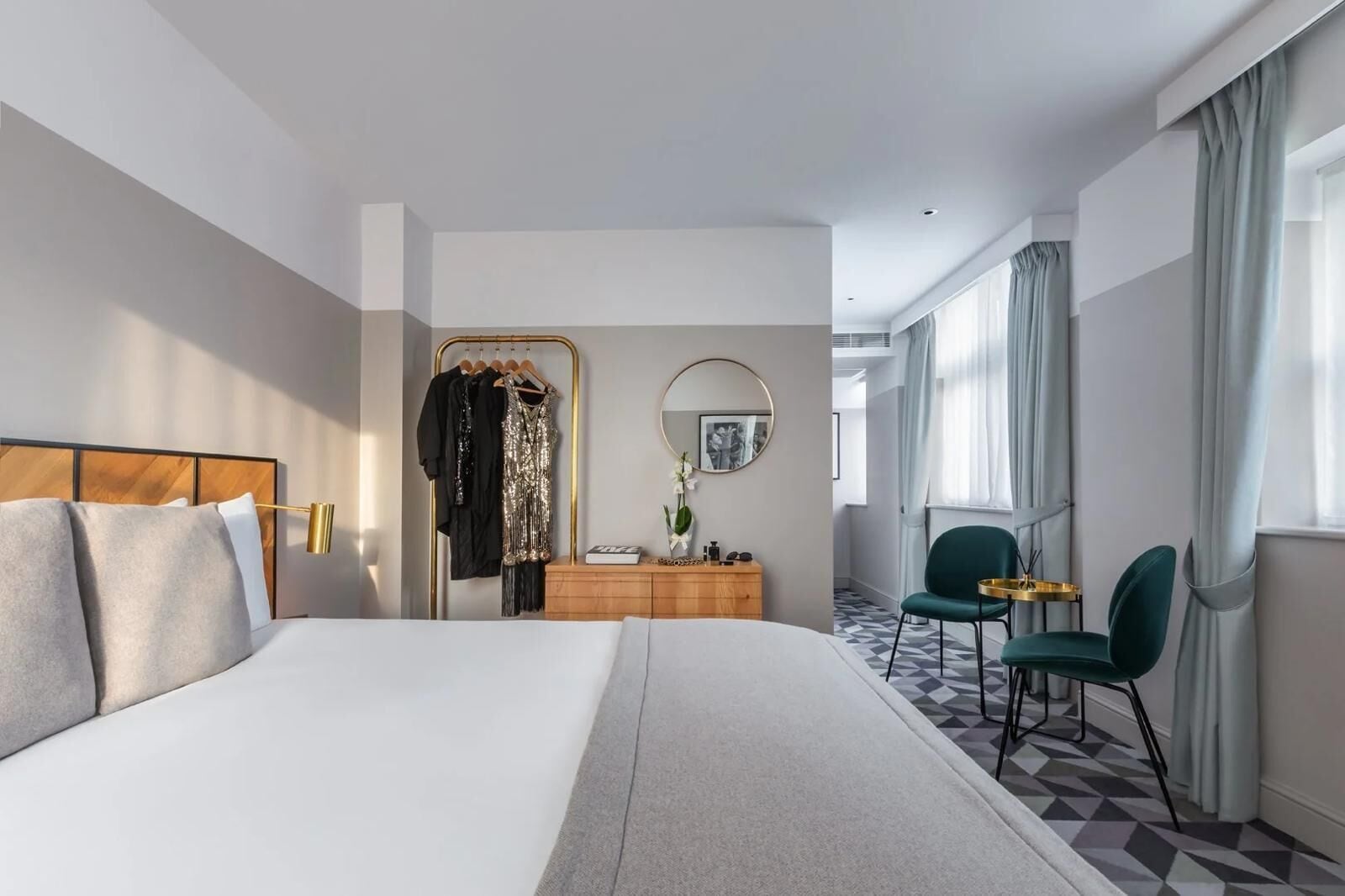 Una habitación de hotel moderna con una cama grande, un aparador, un tocador y un área de descanso con una silla y una mesita.