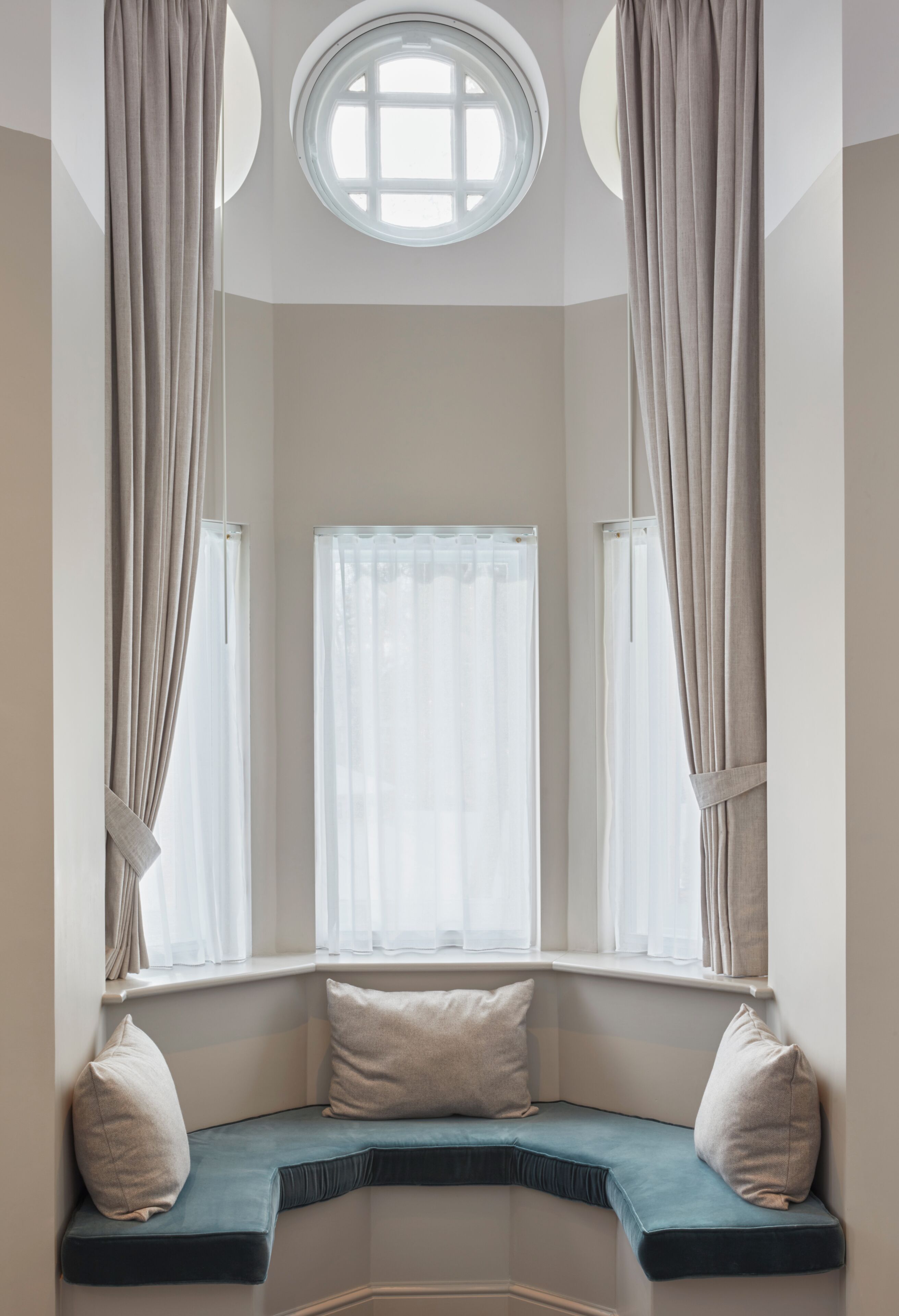 A room with a built-in bench seat, a window with curtains, and a circular skylight.
